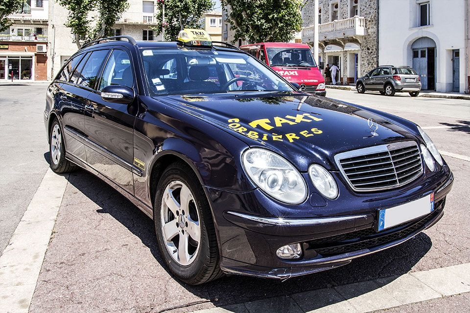 Un taxi bleu foncé est garé dans une rue ensoleillée,