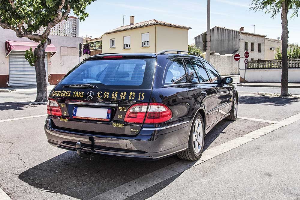 Break noir garé dans la rue. Bâtiments et arbres en arrière-plan. Numéro de téléphone d'un service de taxi sur la vitre.