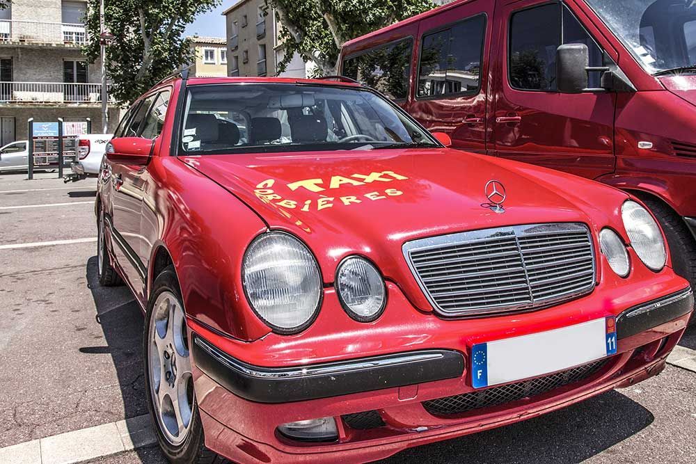 Un taxi rouge est stationné sur un parking, avec l'inscription « TAXI SCIENCE » sur le capot. Une camionnette rouge se trouve à droite.