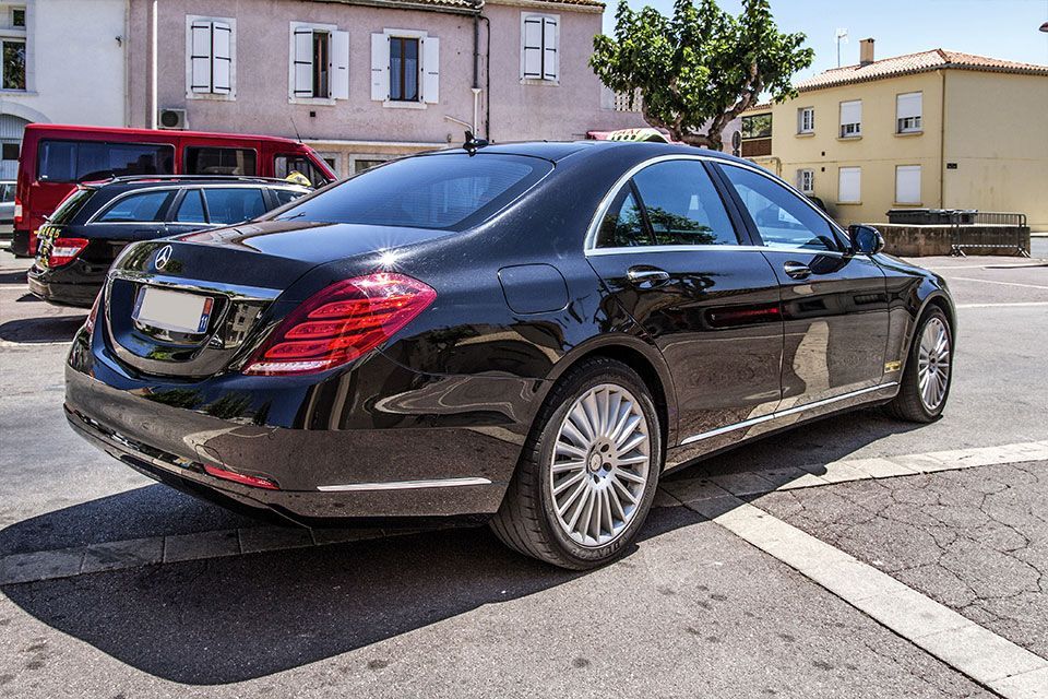 Une berline Mercedes-Benz noire est garée dans une rue, avec d'autres voitures et des bâtiments en arrière-plan.