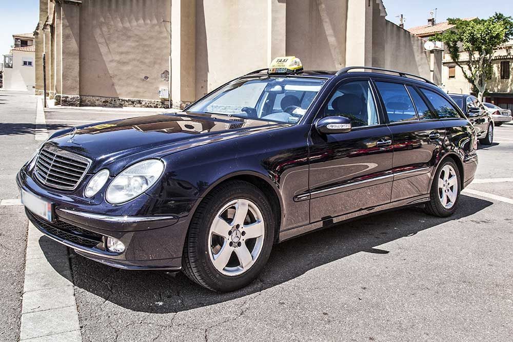 Un taxi Mercedes-Benz break bleu foncé est stationné dans une rue ; un gyrophare est allumé sur le toit.