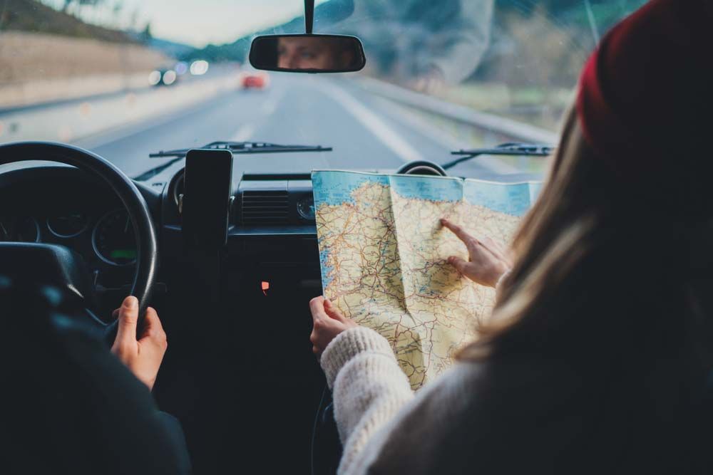 La personne assise côté passager désigne une carte à l'intérieur d'une voiture en mouvement.