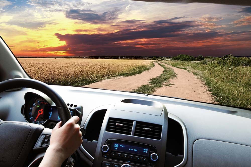 La main sur le volant, je conduis sur un chemin de terre à travers un champ au coucher du soleil.