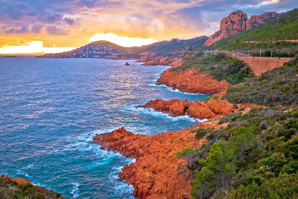 Vue côtière avec des falaises de roche rouge, une eau turquoise et un ciel au coucher du soleil.