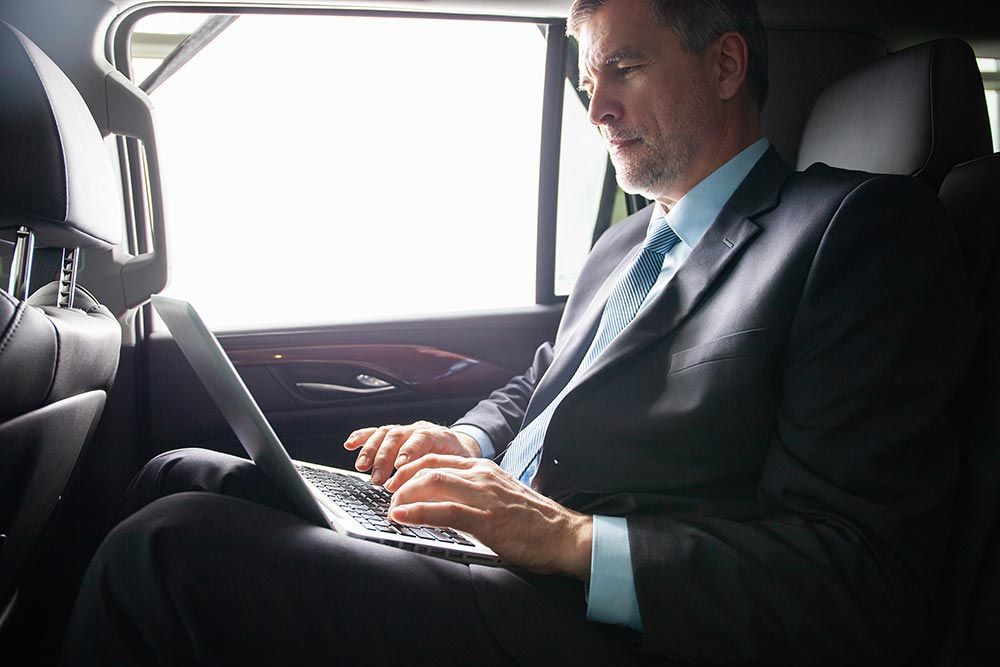 Un homme en costume travaille sur un ordinateur portable sur la banquette arrière d'une voiture.