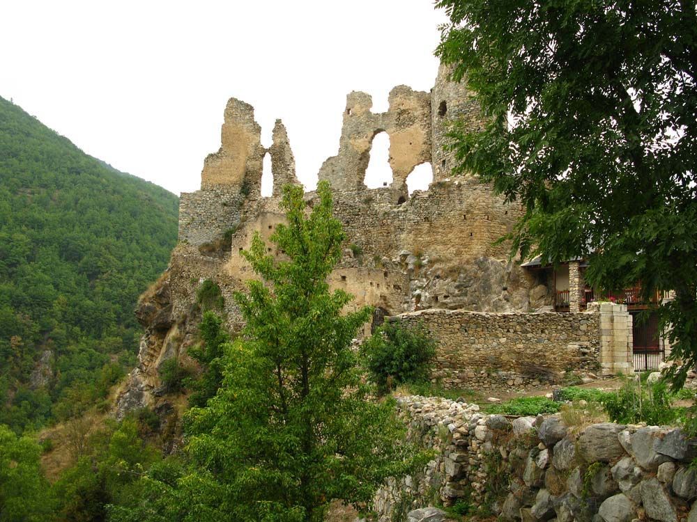 Château de pierre en ruines sur une falaise rocheuse, collines verdoyantes en arrière-plan.