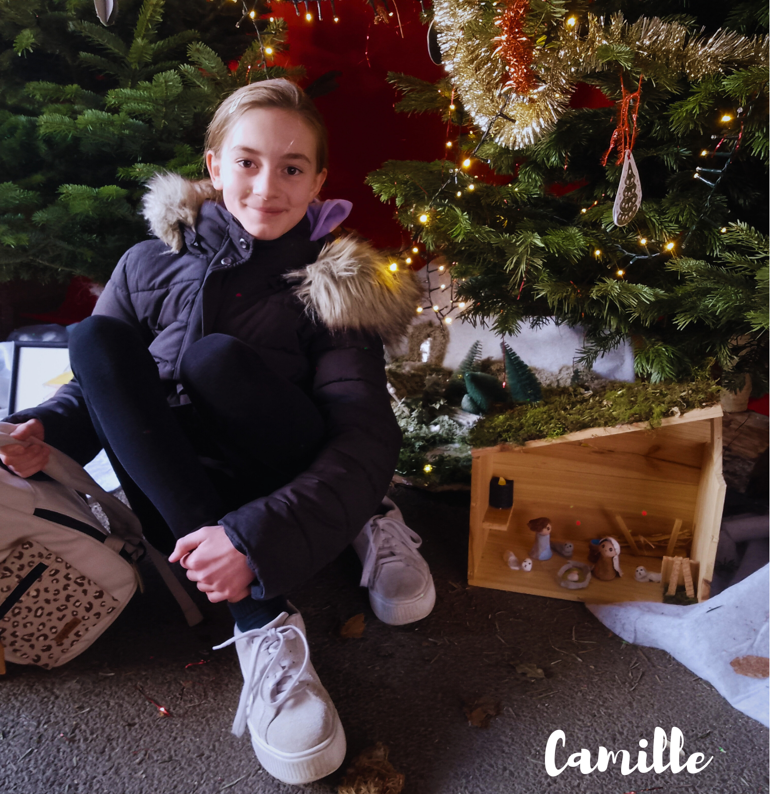 Un garçon assis devant un sapin de Noël et une crèche
