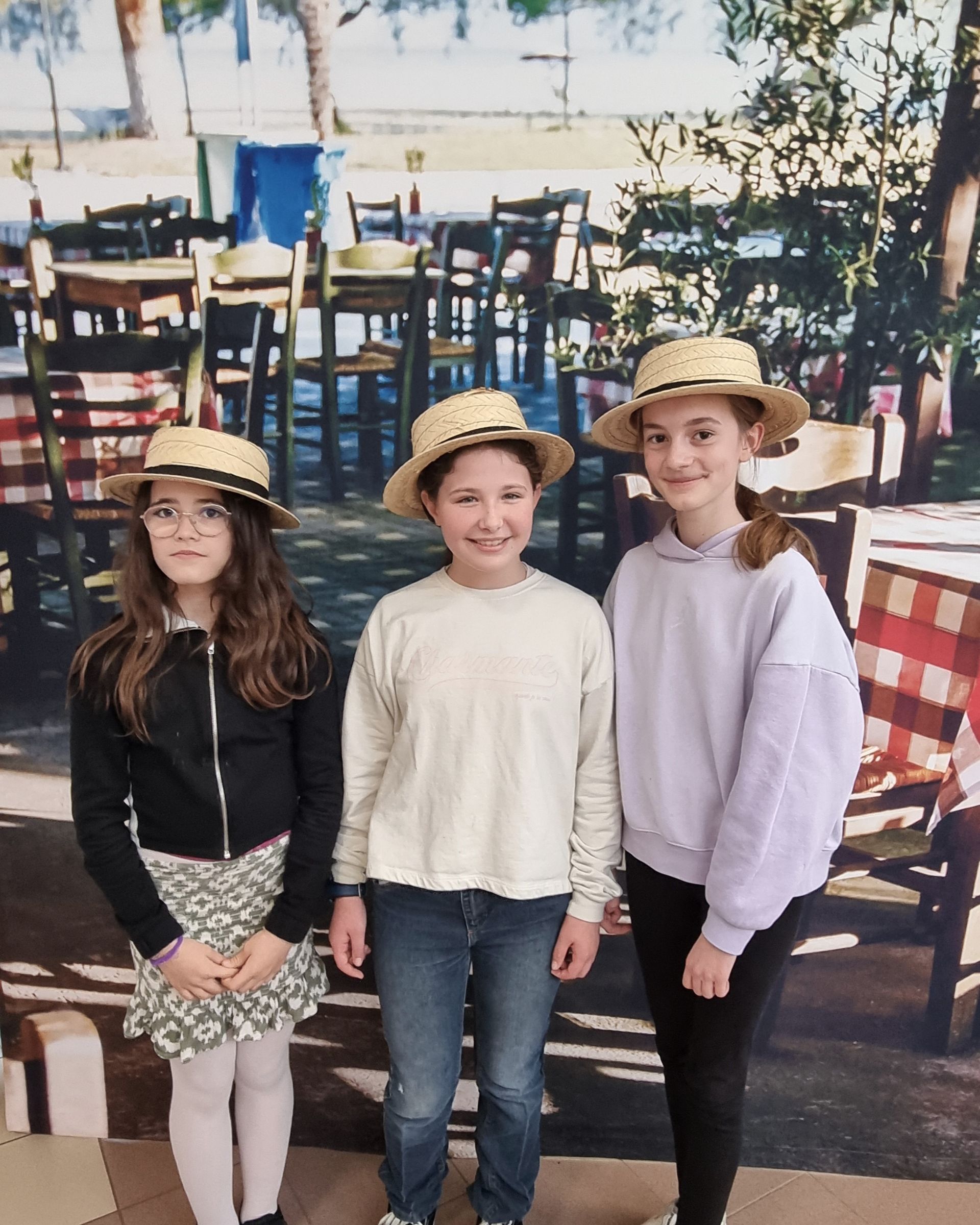 Trois collégiennes qui portent un chapeau de pailles devant une photo avec des tables