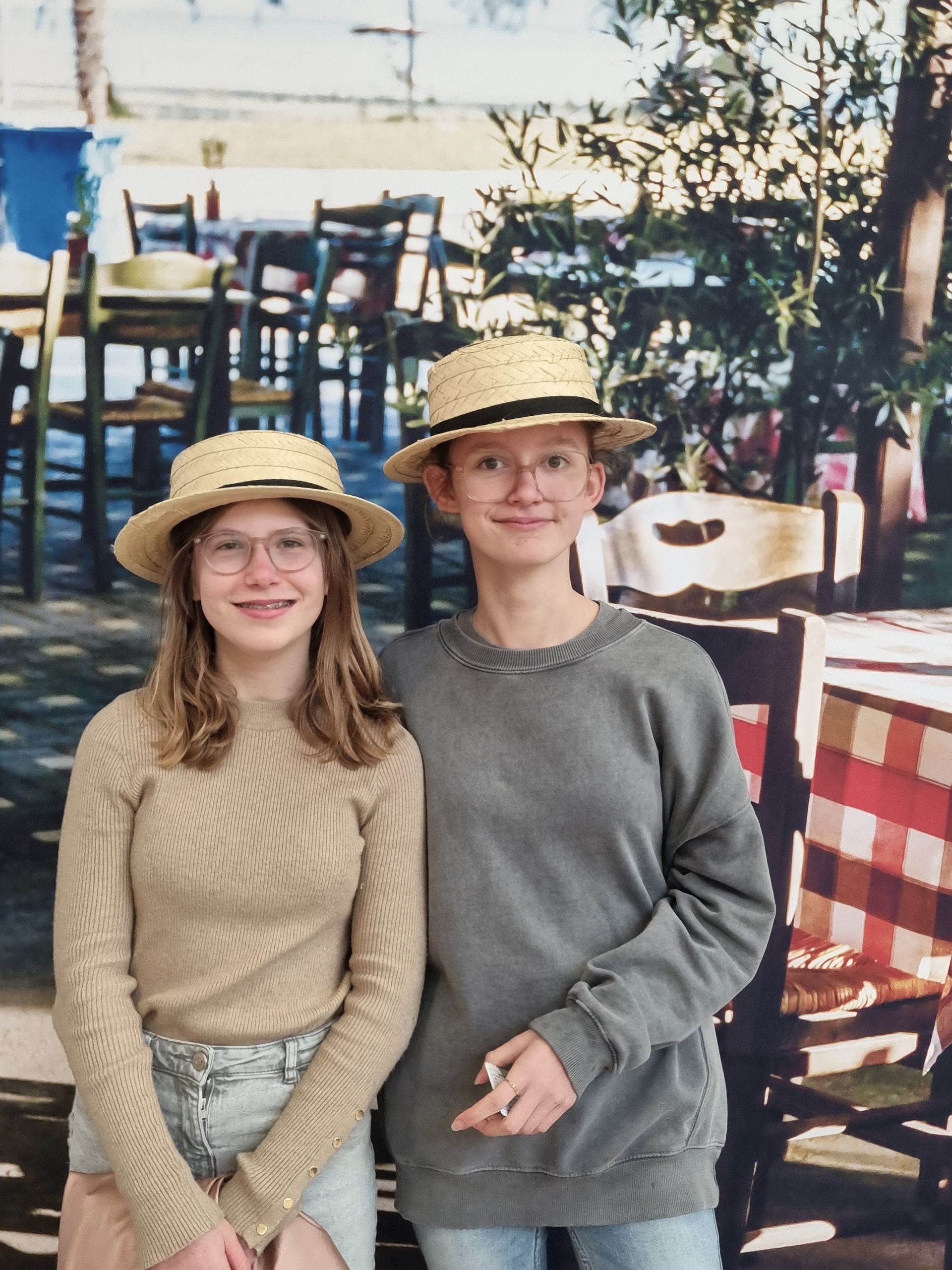 Deux collégiens prenant la pose devant une photo de chaises en bois et une nappe à carreaux