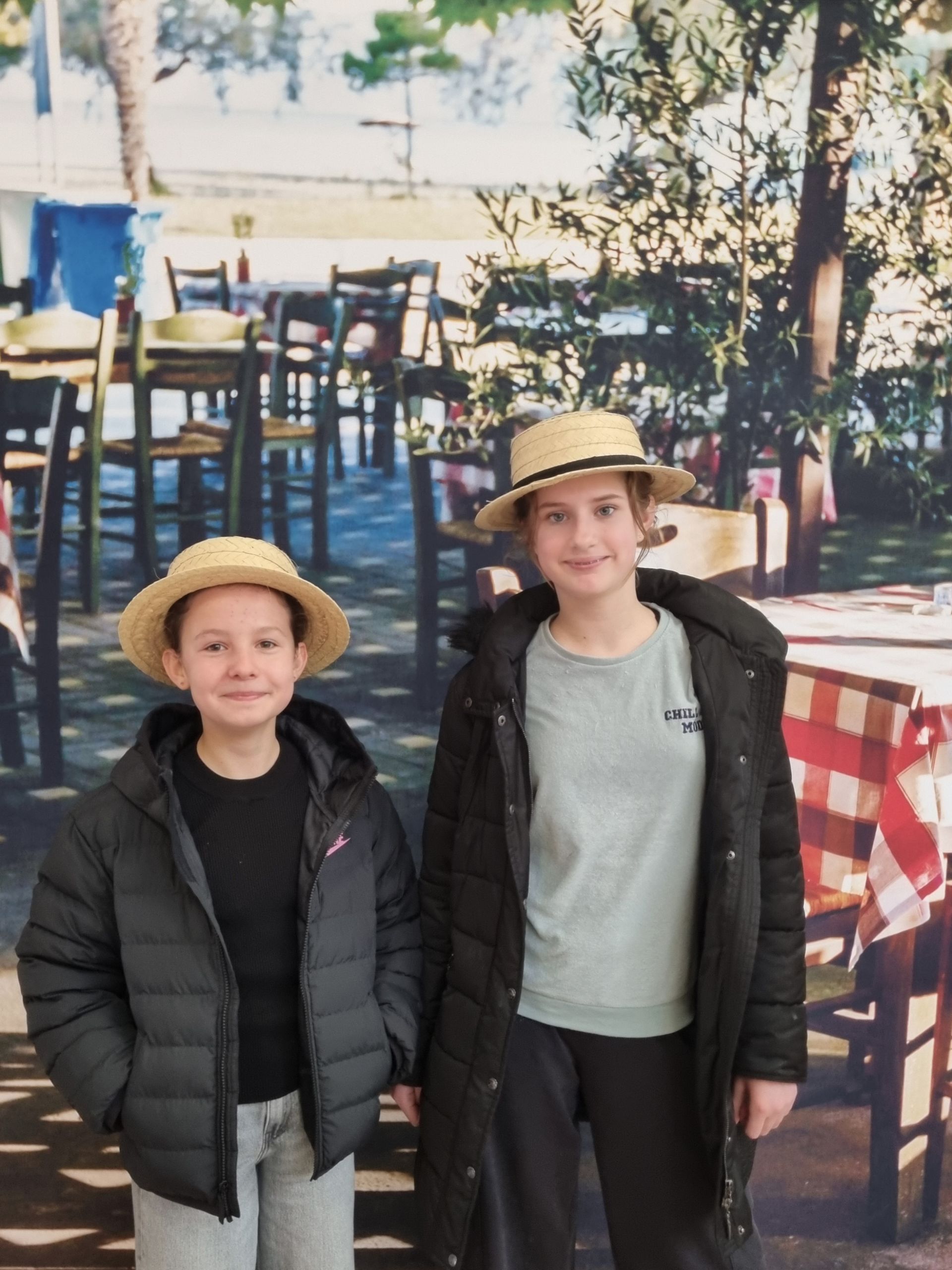 Deux élèves qui prennent la pose devant une photo avec des chaises en bois et une nappe à carreaux