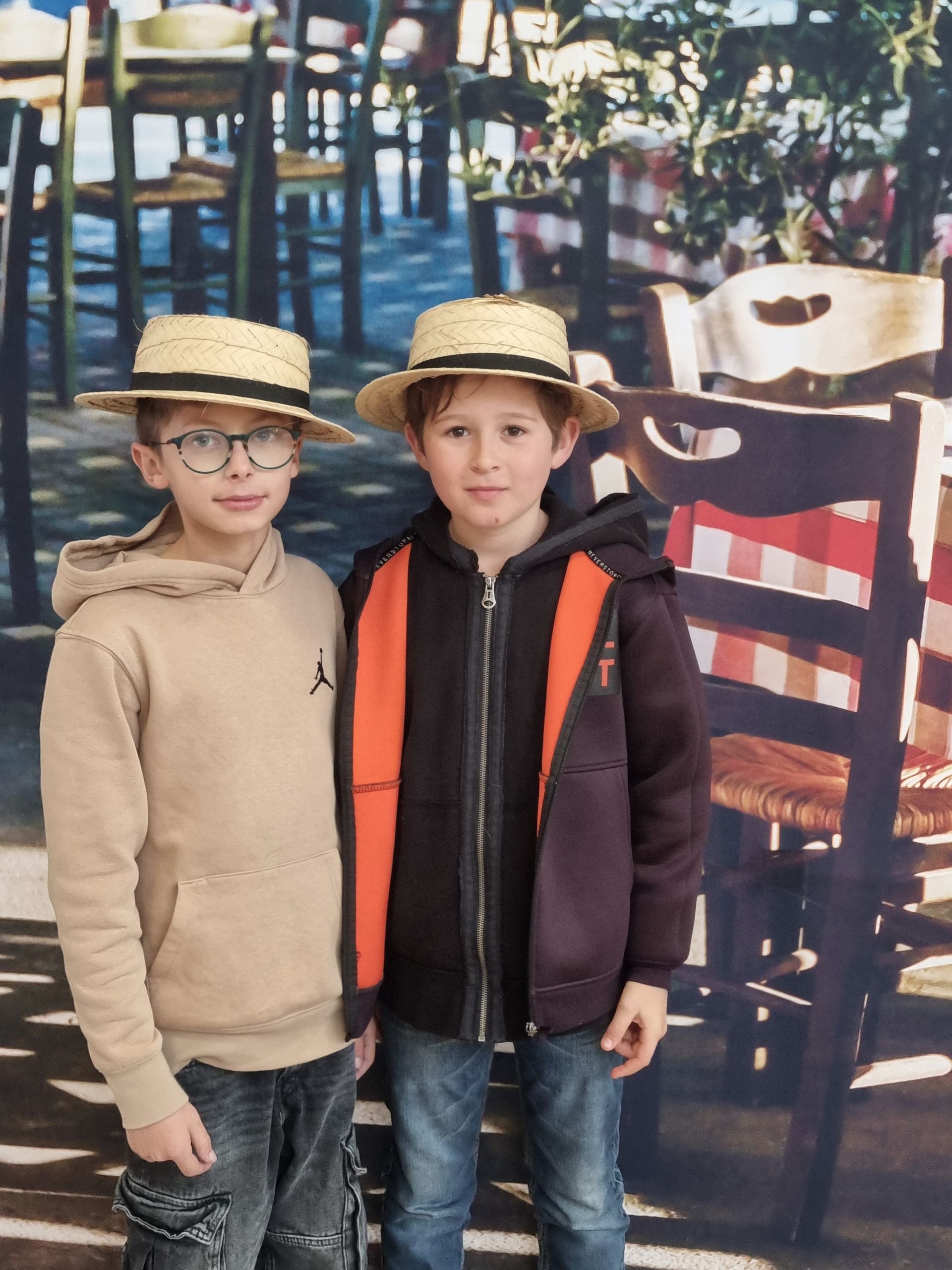 Deux garçons portant des chapeaux en pailles devant une chaise et une table
