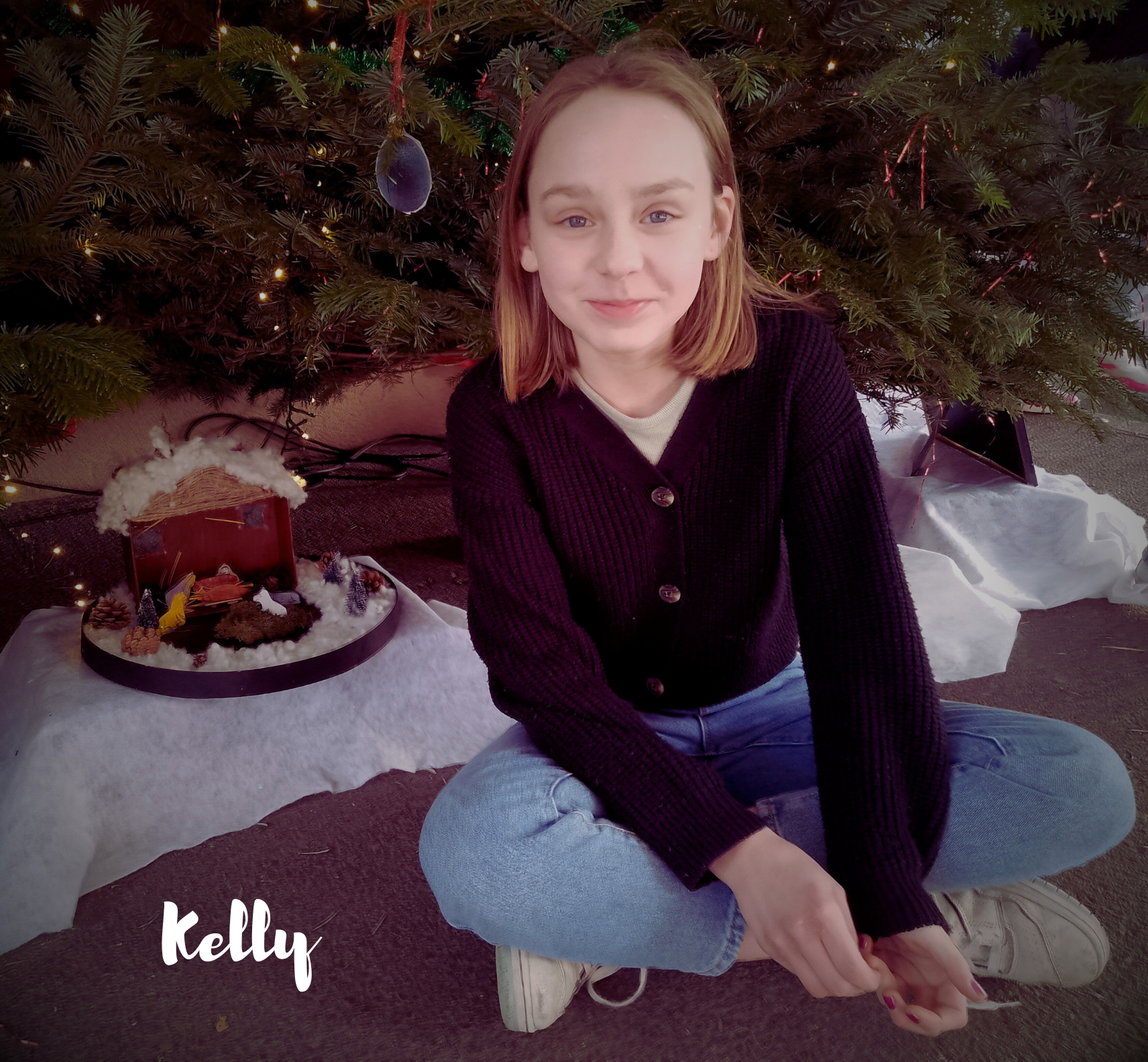 Une fille assise devant un sapin de Noël et une crèche