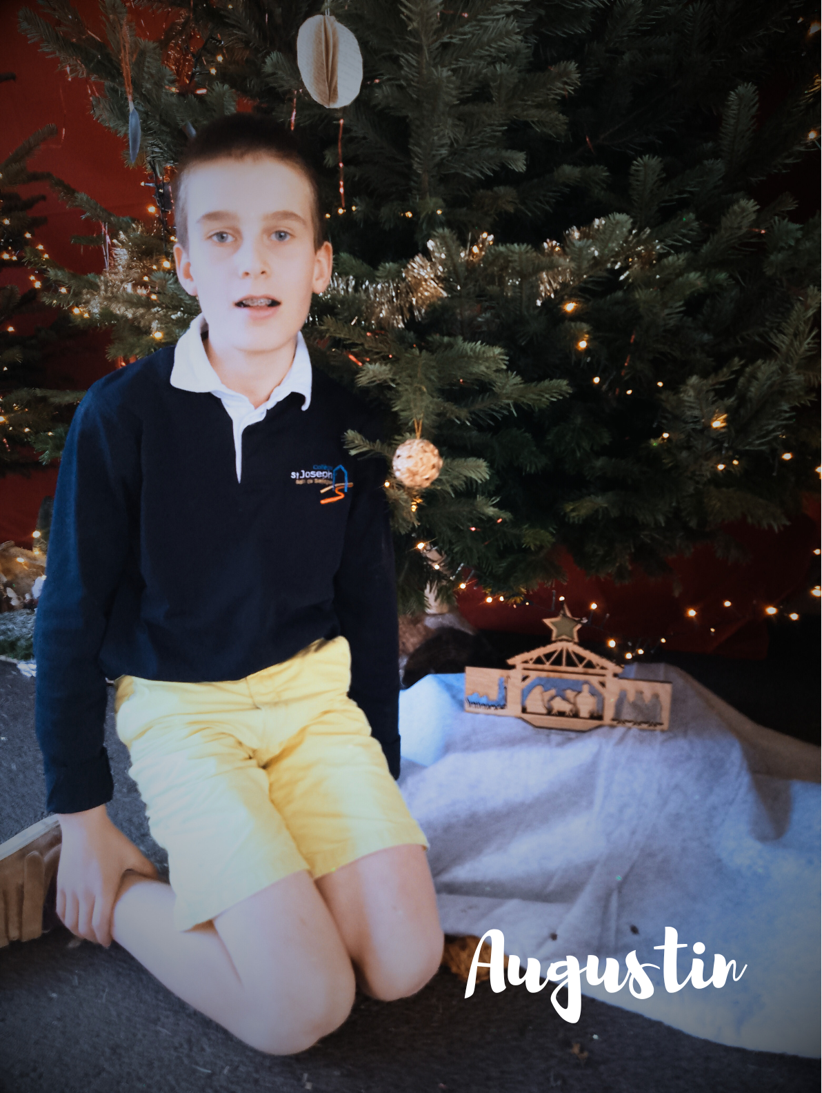 Un enfant assis devant un sapin de Noël et une crèche