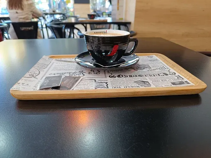 Taza de café en bandeja con estampado de periódico. Taza negra y platillo en bandeja de madera, en interiores.