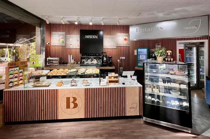 Interior de panadería con exhibición de productos horneados, máquina de café expreso y mostrador de clientes con el logotipo de la empresa visible.