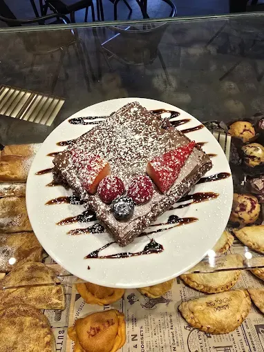 Postre de chocolate con fresas, arándanos, azúcar en polvo y llovizna de chocolate sobre un plato blanco.