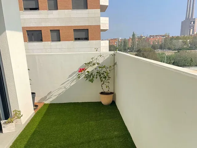 Un balcón con césped artificial y una planta en maceta.