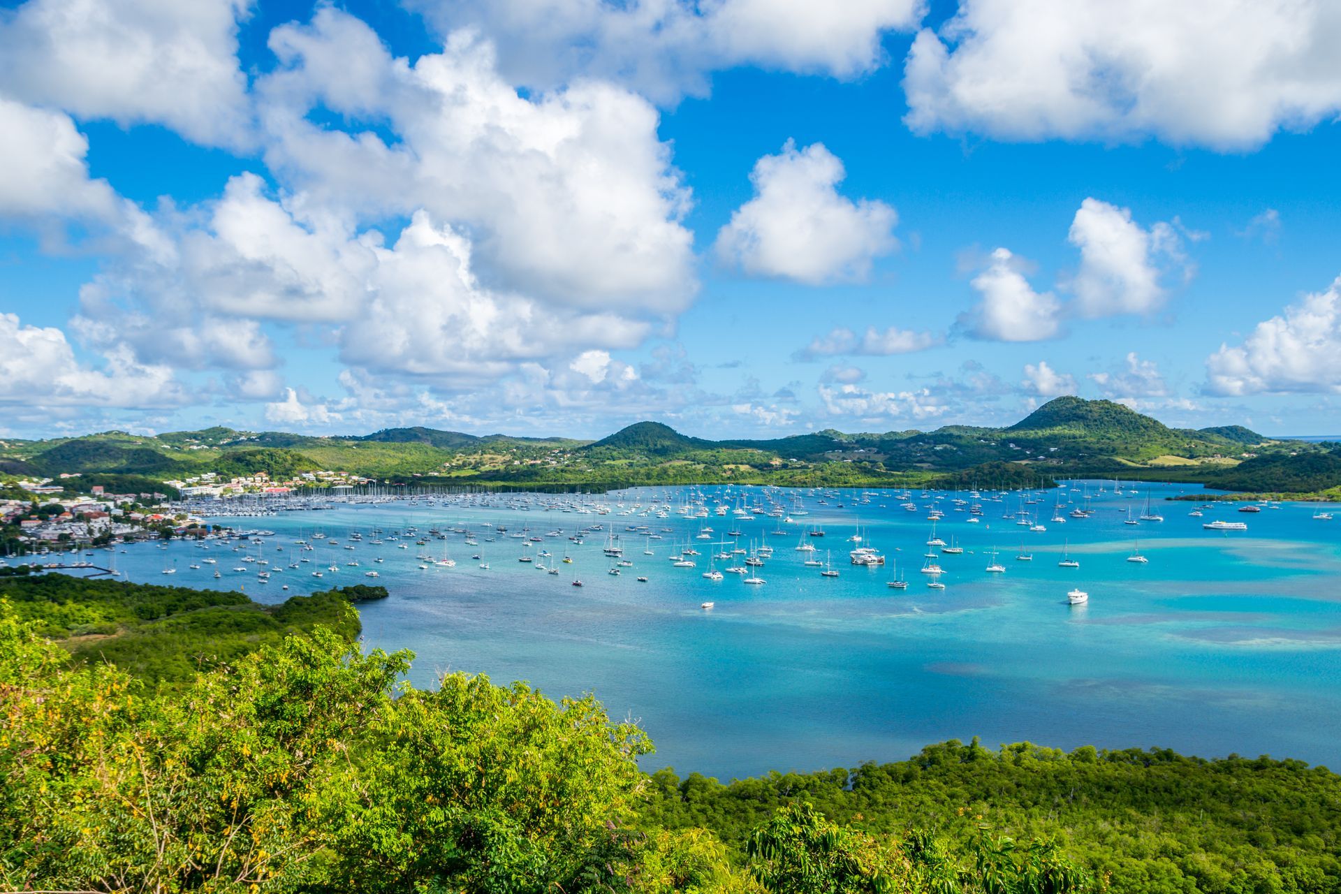 Baie tropicale aux eaux turquoise, bateaux, collines verdoyantes et ciel bleu parsemé de nuages