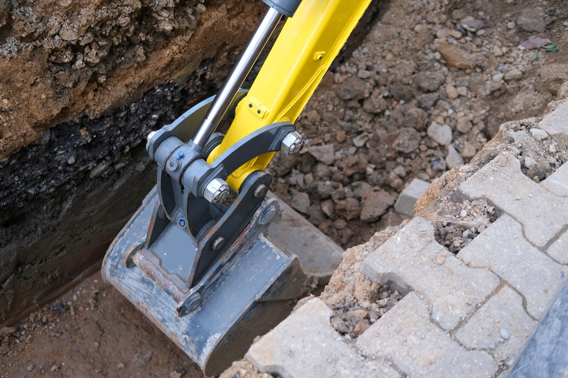 Godet jaune d'une excavatrice creusant le long d'une bordure pavée et d'une tranchée