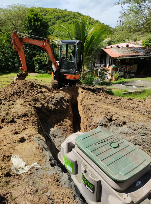 Une excavatrice creuse une profonde tranchée à côté d'une maison, avec un gros appareil enfoui dans la terre.