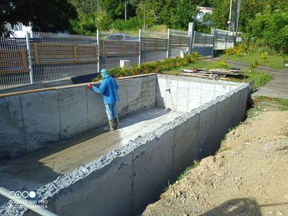 Une personne vêtue d'un vêtement bleu se tient dans un caniveau en béton, au bord d'une route clôturée.