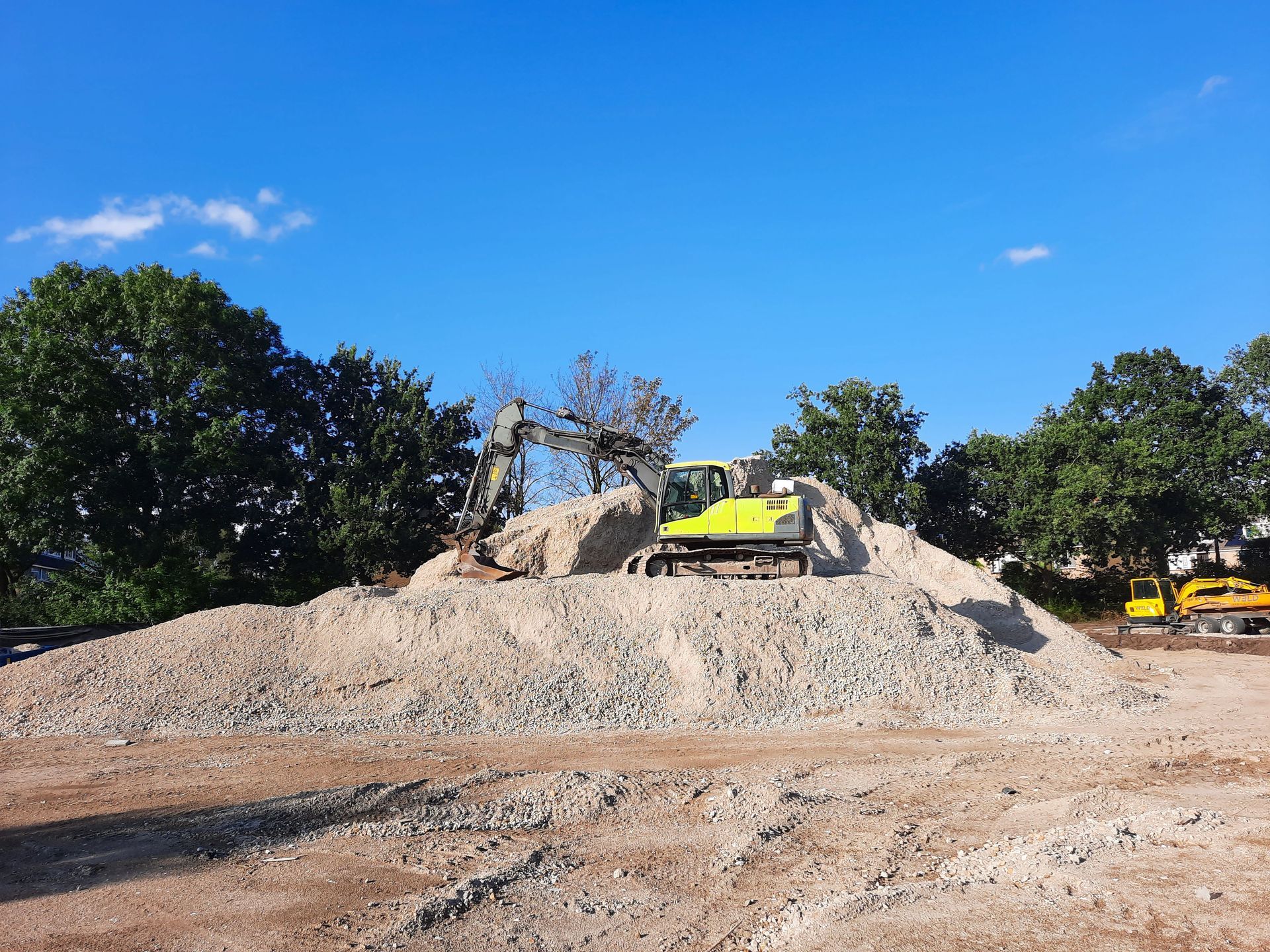 Une pelleteuse jaune au sommet d'un monticule de gravier sur un chantier de construction sous un ciel bleu