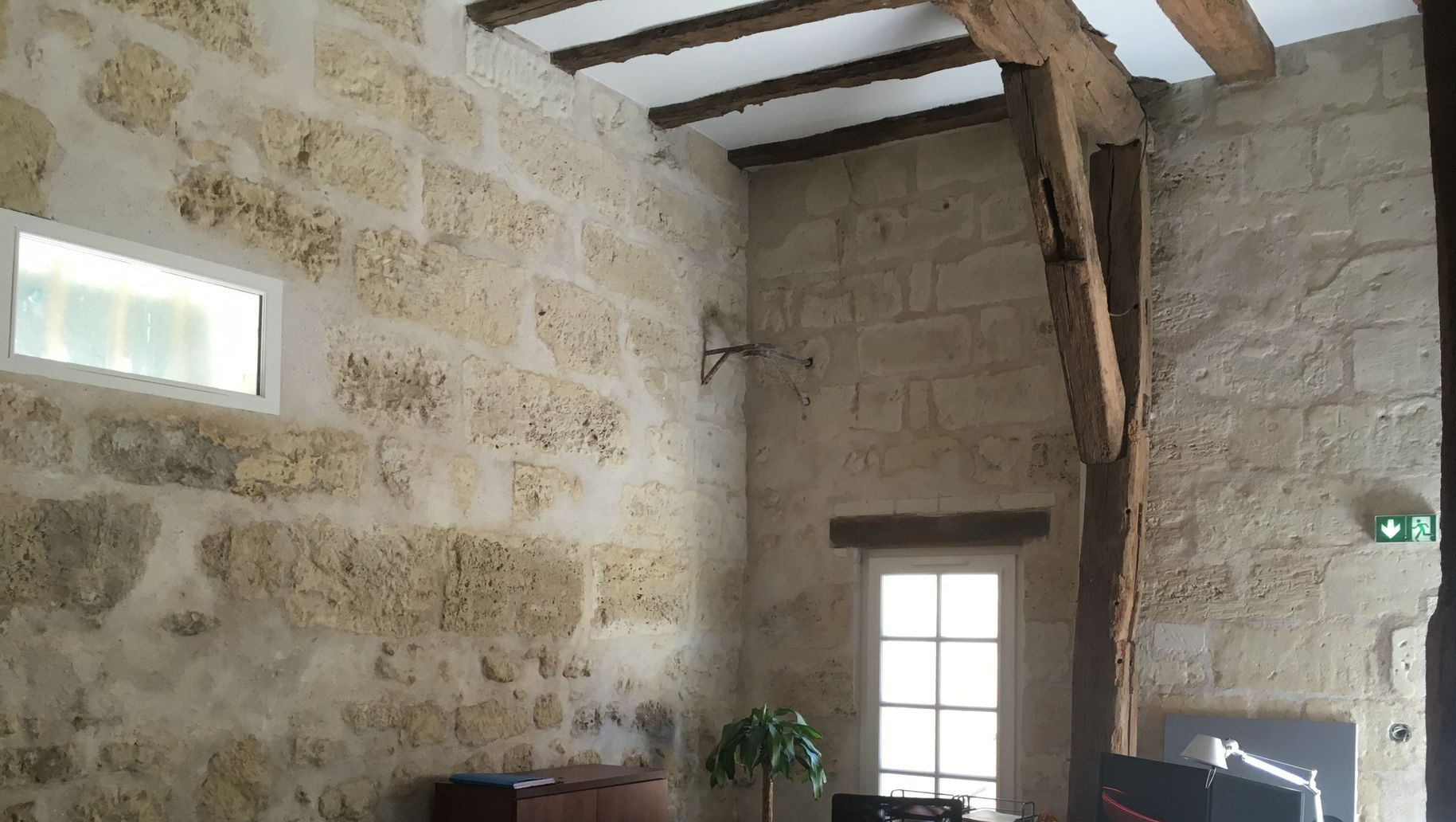 Grande pièce avec une grande hauteur sous plafond comportant un bureau, des poutres et des murs en tuffeau