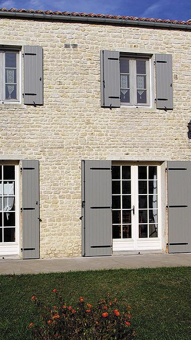 Grande maison en pierre avec fenêtres en PVC et volets en bois.