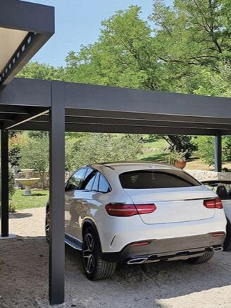 Carport en aluminium protégeant des voitures blanches avec des végétaux en second plan.