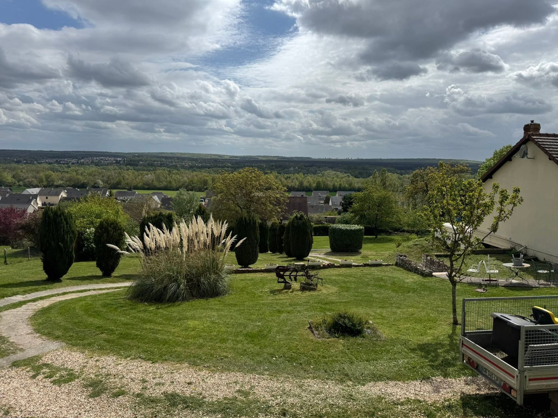 Jardin luxuriant avec pelouse, arbustes et campagne au loin sous un ciel nuageux