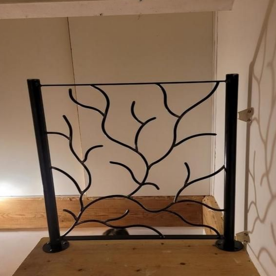 Garde-corps en métal noir avec motif de branches; installé sur une surface en bois.