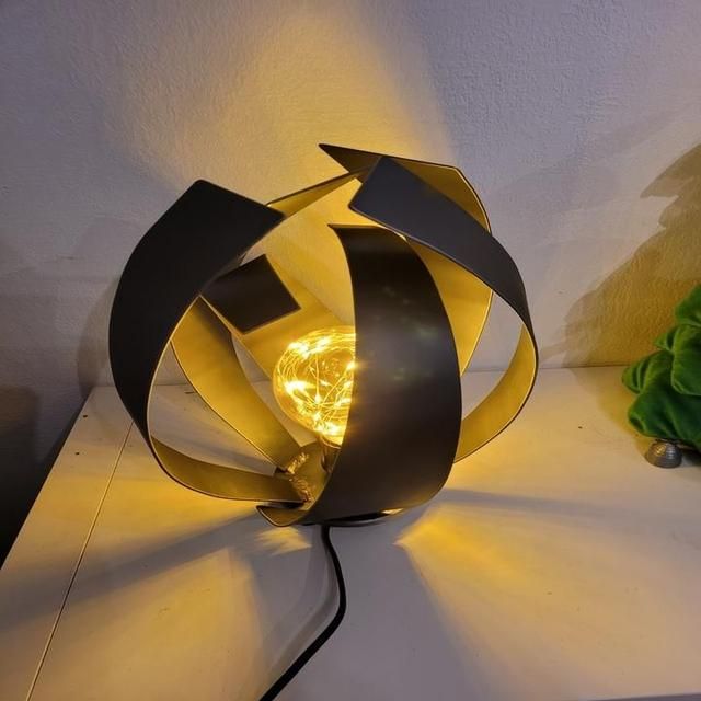Une lampe sphérique dorée et noire avec des guirlandes lumineuses internes.