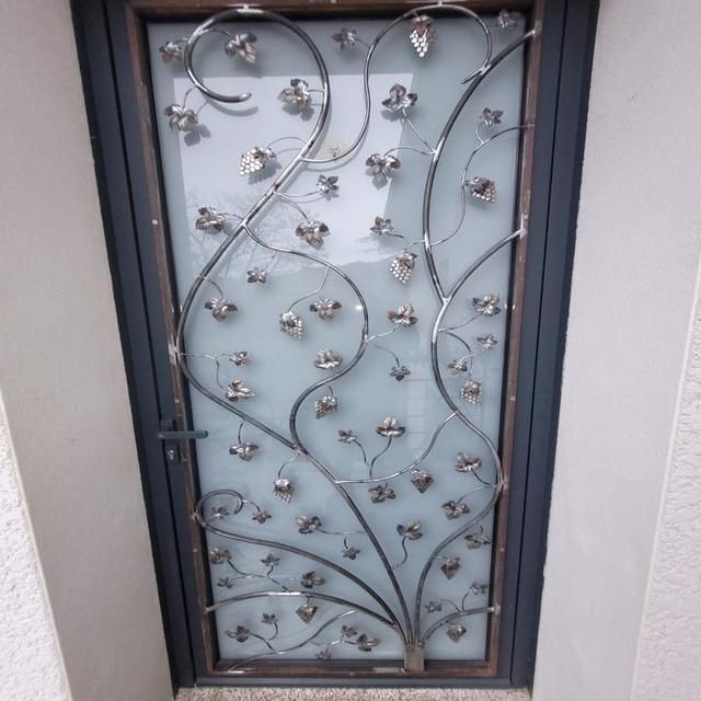 Vignes en fer forgé avec feuilles argentées sur un panneau de fenêtre en verre dépoli. Cadre gris foncé.