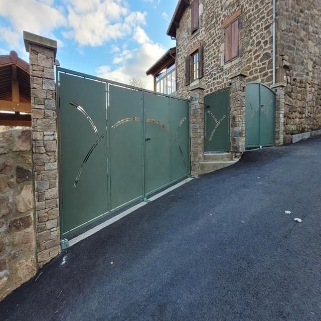 Portail d'allée en métal vert avec découpes décoratives, encastré entre des piliers en pierre.