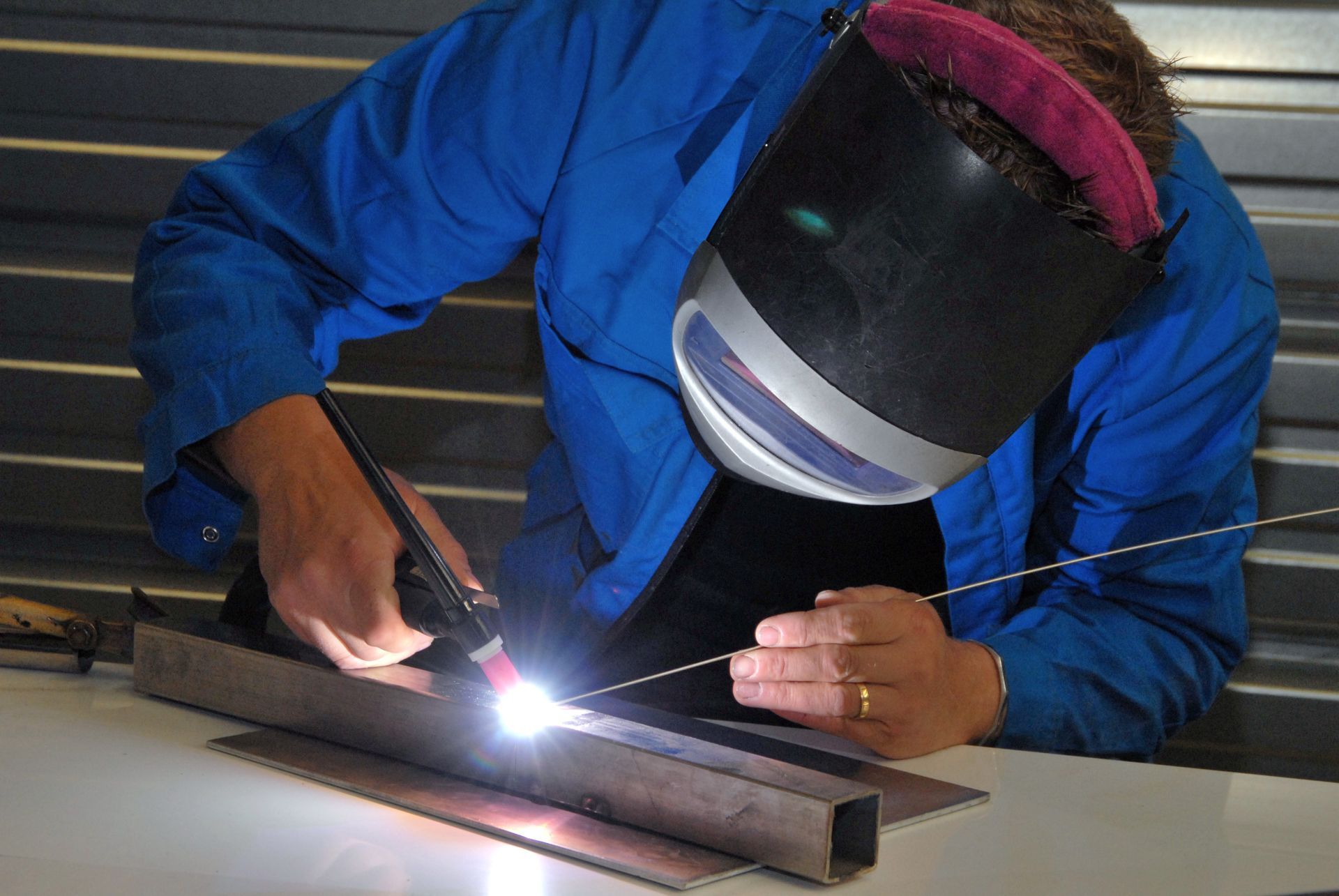 Soudeur en combinaison bleue, soudant du métal avec un arc brillant dans un atelier.
