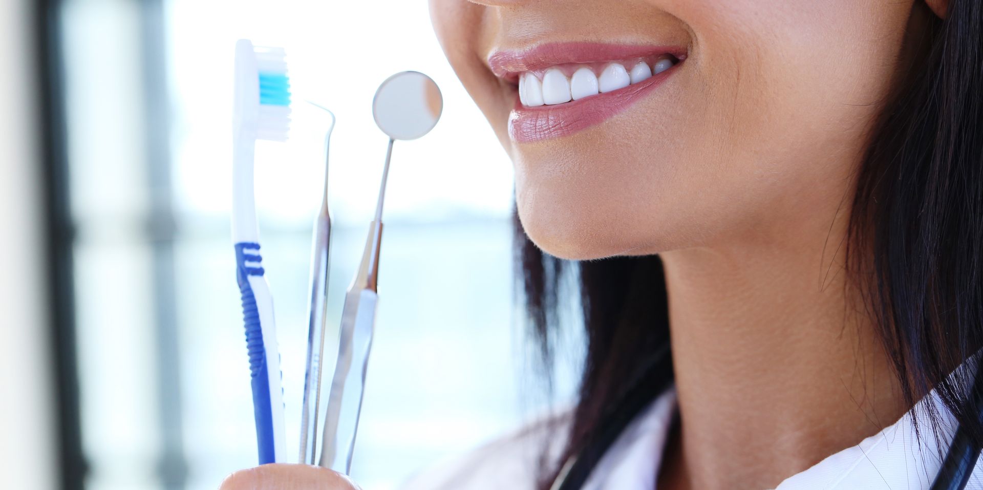 Una dentista sostiene un cepillo de dientes, un espejo e instrumentos dentales.