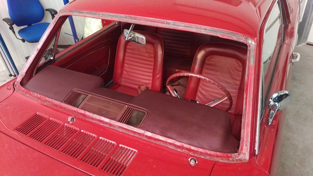 Ein rotes Auto mit kaputter Windschutzscheibe steht in einer Garage.