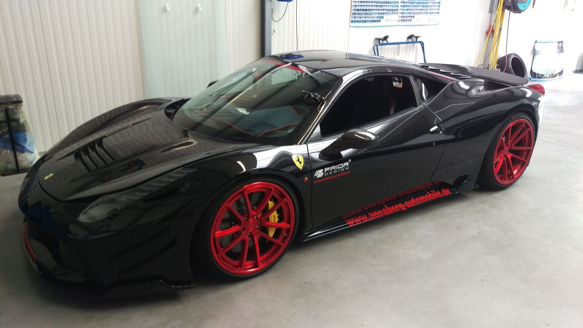 Ein schwarzer Sportwagen mit roten Rädern steht in einer Garage.