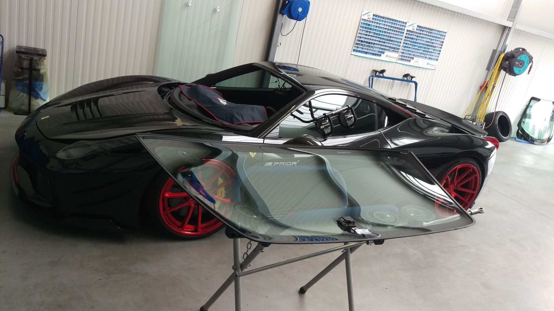 Ein schwarzer Sportwagen mit kaputter Windschutzscheibe steht auf einem Ständer in einer Garage.