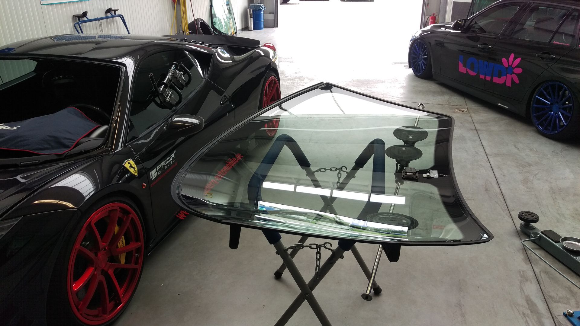 Ein schwarzer Sportwagen mit roten Rädern steht mit einer Windschutzscheibe auf einem Ständer in einer Garage.