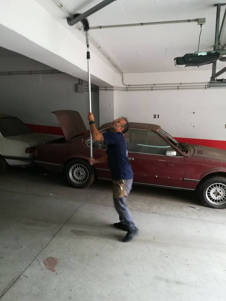 Un hombre sostiene un poste en un garaje al lado de un coche rojo.