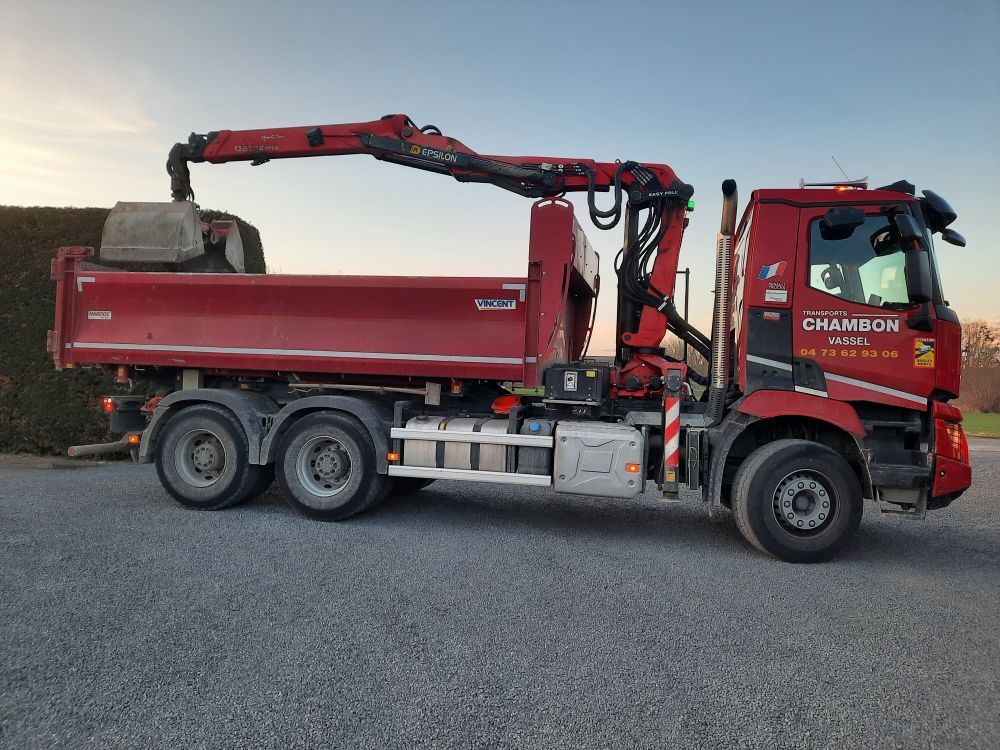 Camion à benne basculante rouge avec grue chargeant du matériel sur le lit contre un ciel bleu.