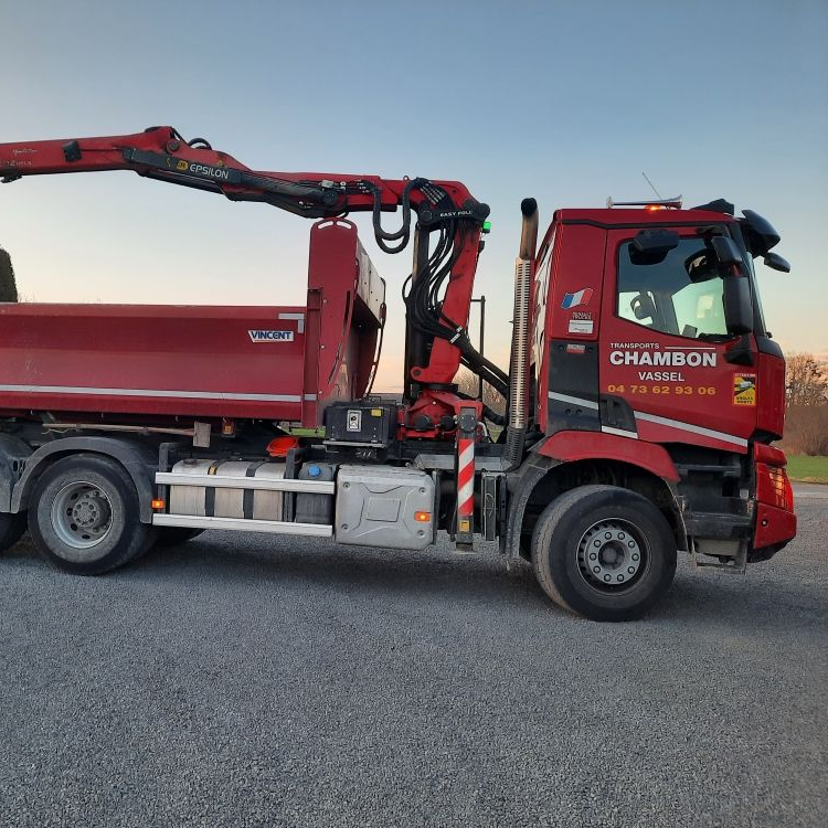Camion de construction rouge avec grue, stationné sur du gravier.