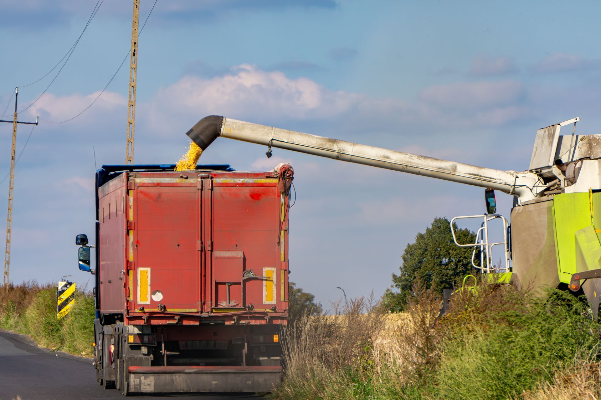 Moissonneuse-batteuse déchargeant du grain dans un camion rouge sur une route rurale.