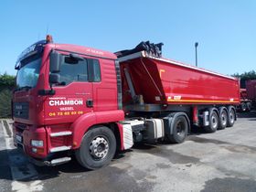 Camion MAN rouge avec remorque, garé sur le trottoir. La remorque est surélevée ; ciel bleu.