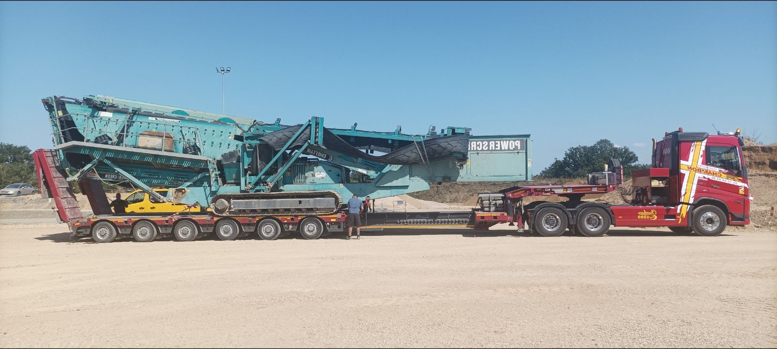 Une grosse pièce de machine industrielle transportée par un camion rouge par une journée ensoleillée.