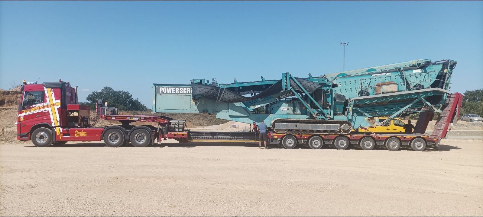 Une grande machine industrielle de couleur bleu sarcelle sur la remorque d'un camion rouge