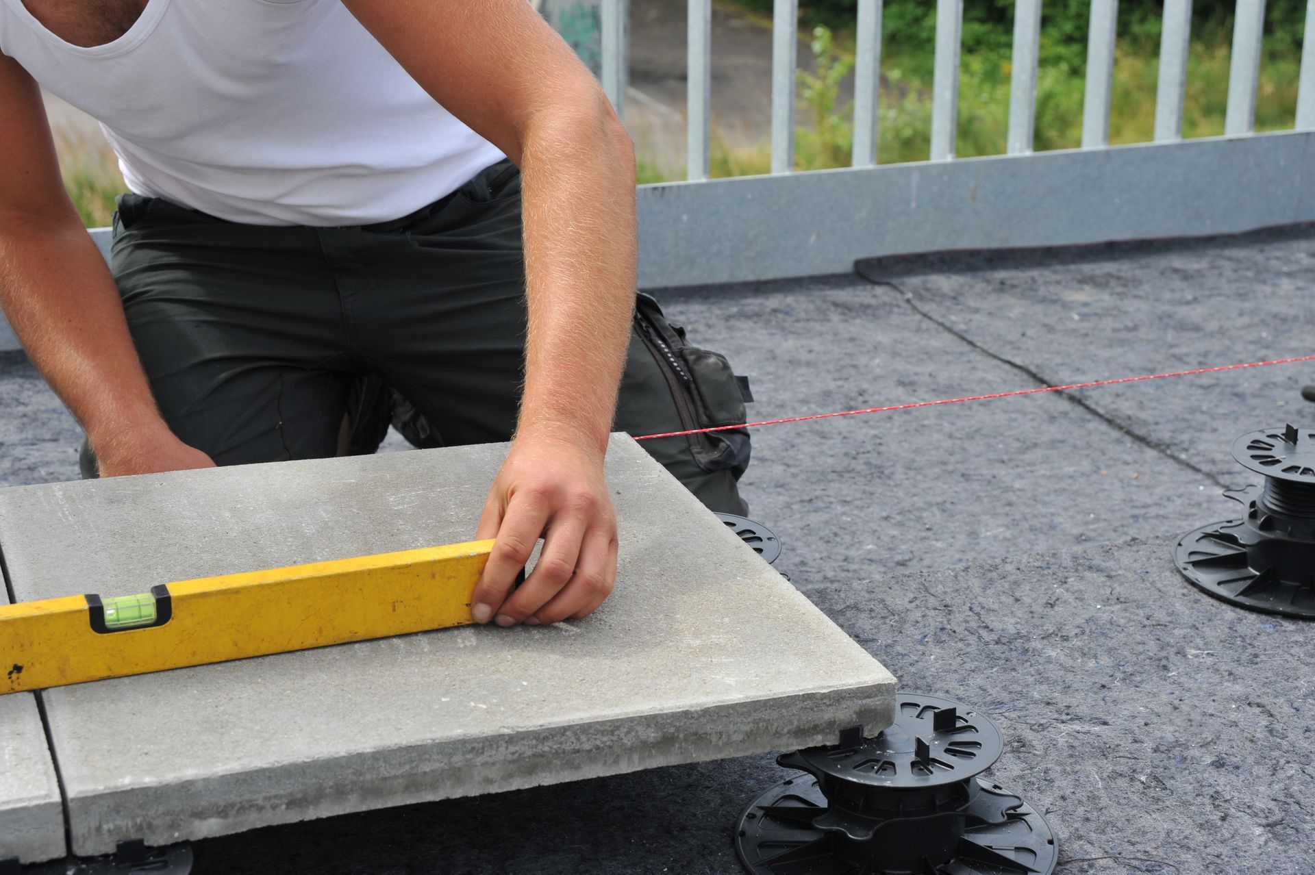 Une personne nivelle une dalle de béton à l'aide d'un niveau à bulle jaune sur un toit-terrasse.