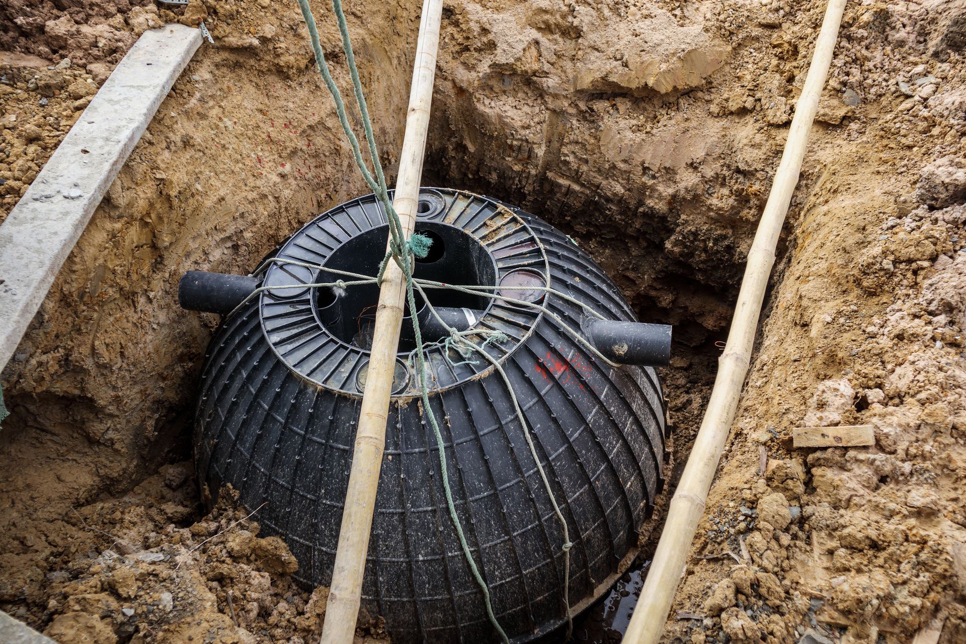 Cuve noire ressemblant à un réservoir, située dans une excavation, entourée de tuyaux et de cordes.