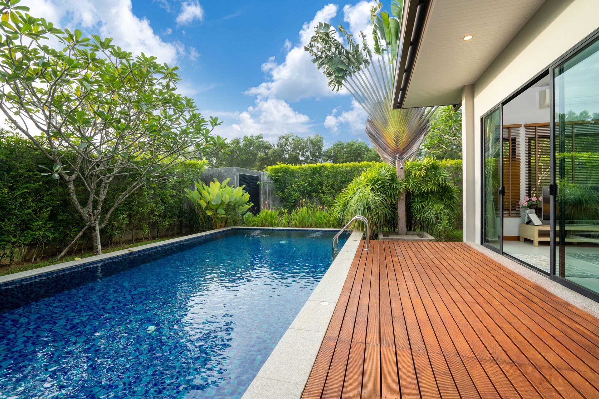 Patio moderne avec terrasse en bois donnant sur une piscine bleue et un jardin luxuriant